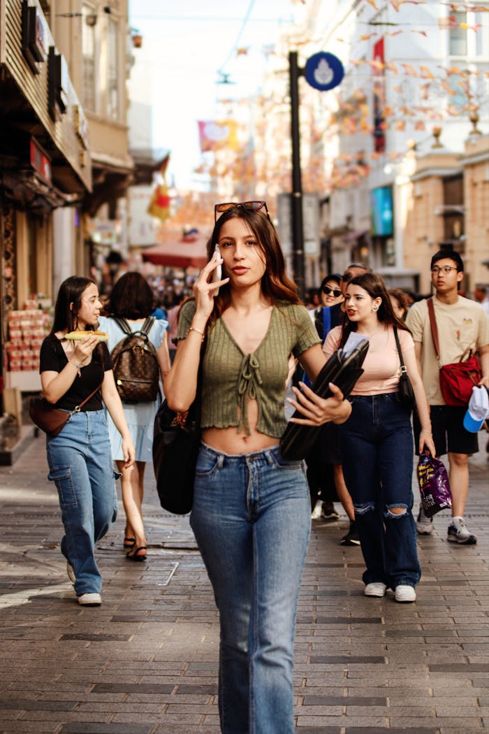 A stylish woman walks in a vibrant urban street, surrounded by people enjoying the lively city environment.